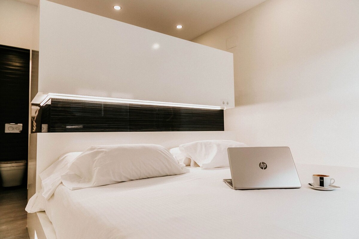 A modern hotel room with a bed, a laptop, and a cup on a table.
