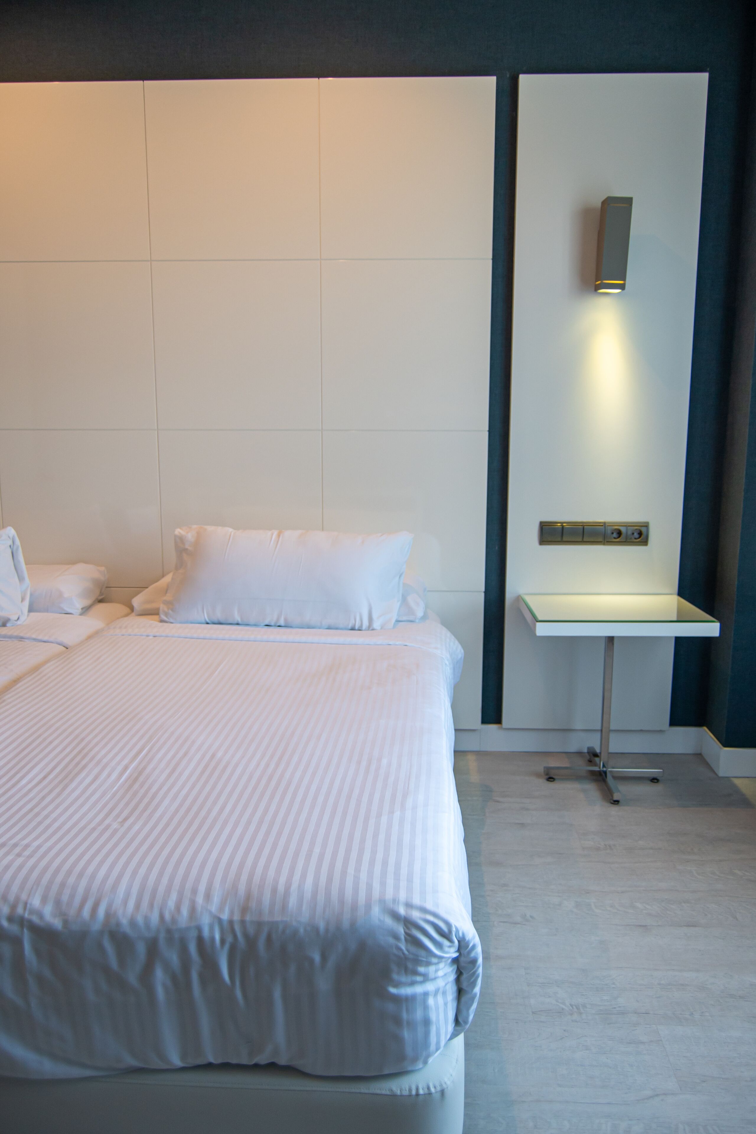 Una habitación de hotel moderna con una cama grande, una mesita de noche y una lámpara fijada a la pared.