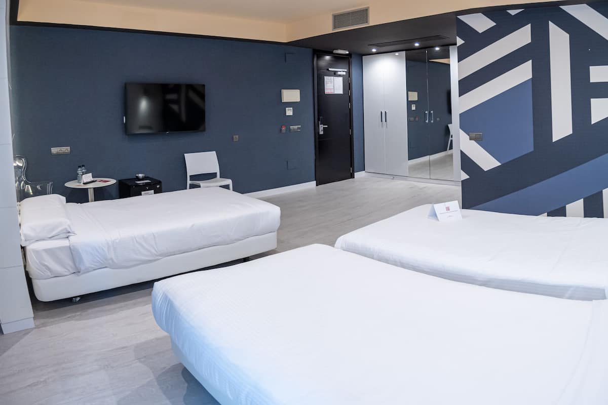 A hotel room with two beds, a TV, a small table with a chair, and a mirror.