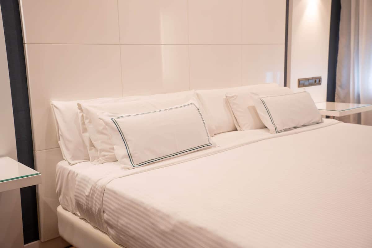 A neatly made bed with white linens and a glass bedside table.