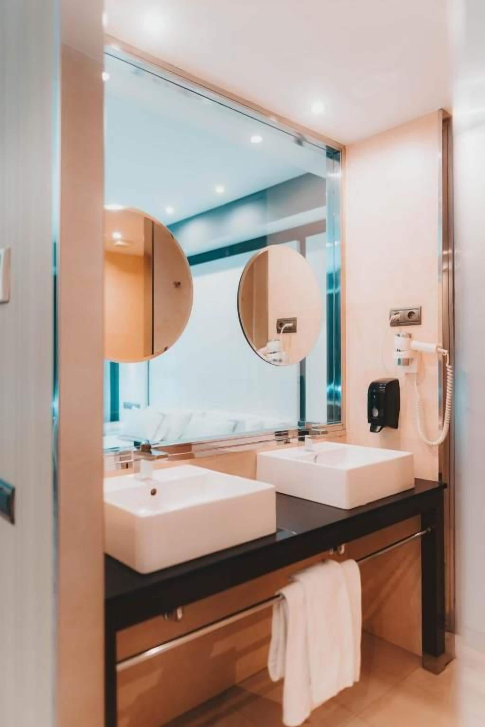 Une salle de bain moderne avec deux lavabos, un grand miroir et une douchette à main.