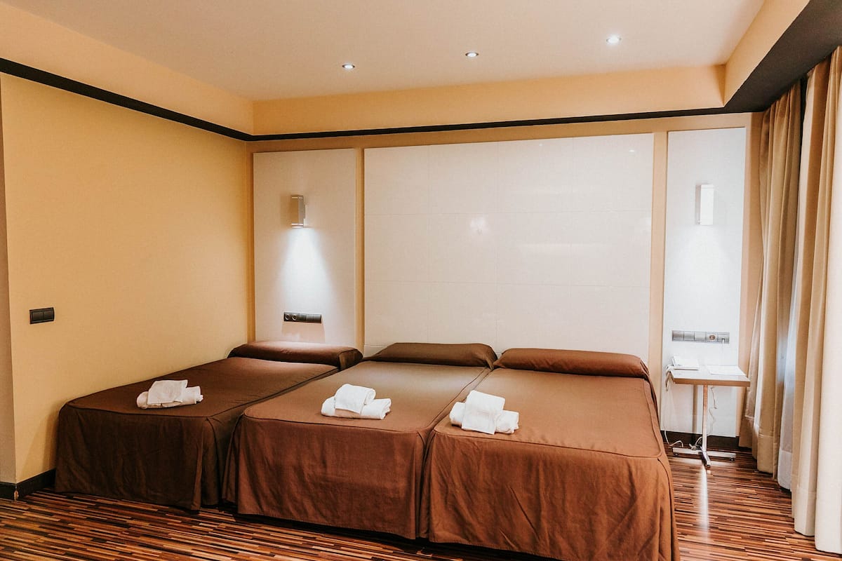 A hotel room with two beds, a small table, and a window with curtains.