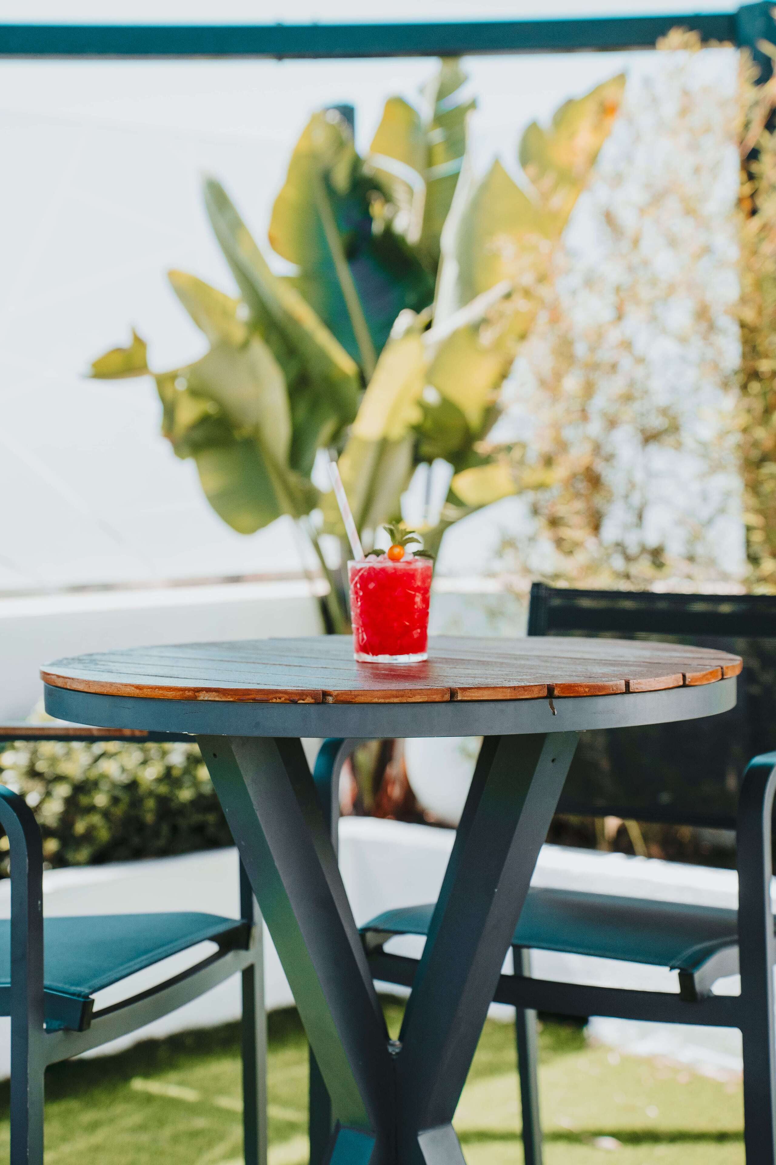 Une table ronde avec une boisson dessus, entourée de chaises, dans un cadre extérieur agrémenté de verdure.