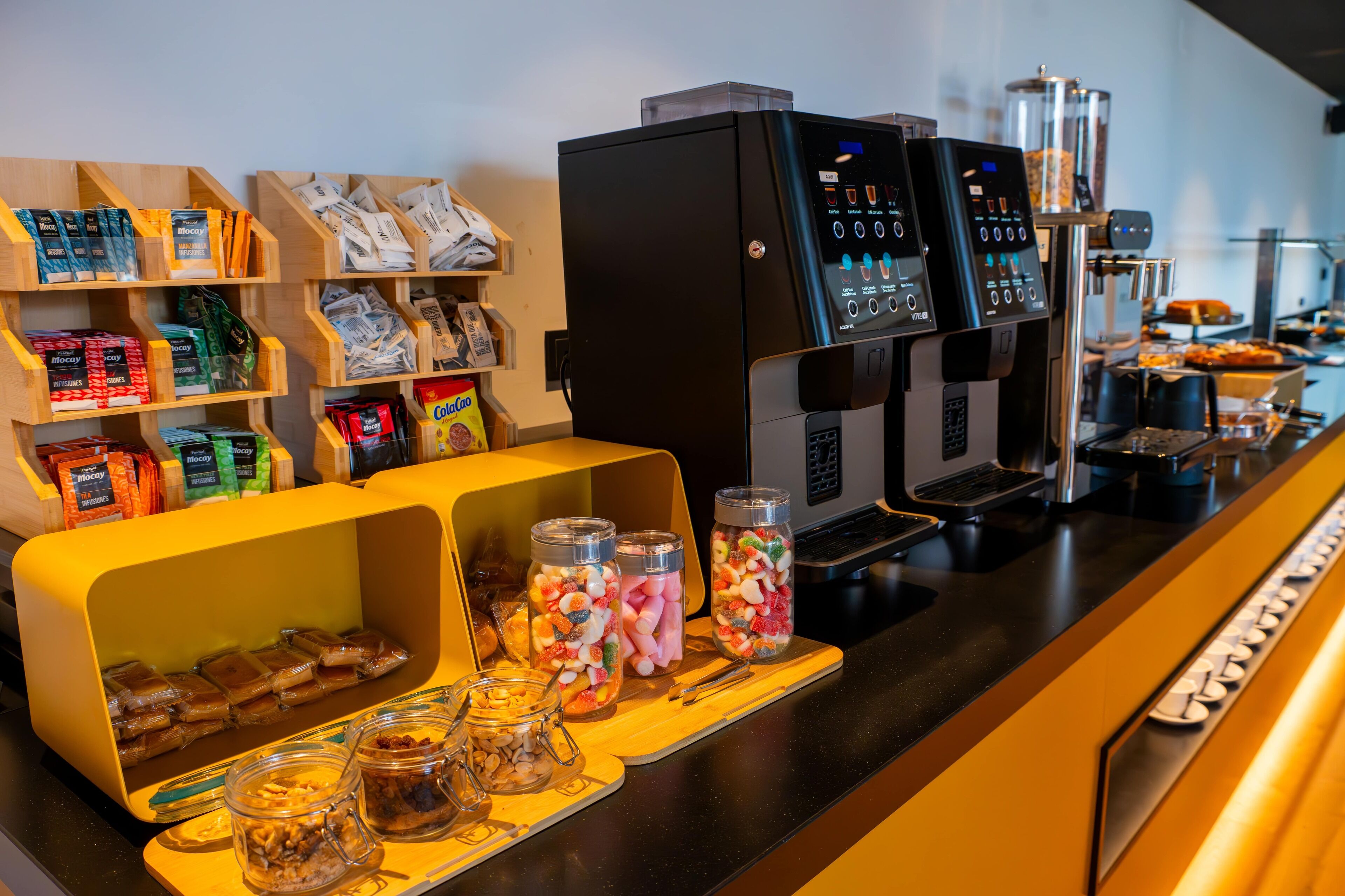 Eine Kaffeestation mit einer Kaffeemaschine, Snacks in Gläsern und verpackten Lebensmitteln.