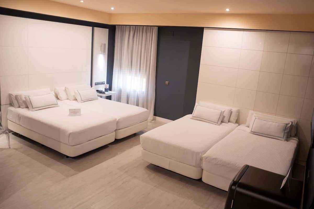 A hotel room with two beds, a desk, a chair, and a small table.