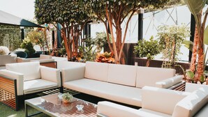 An outdoor seating area with a white sofa, striped coffee table, and various potted plants.