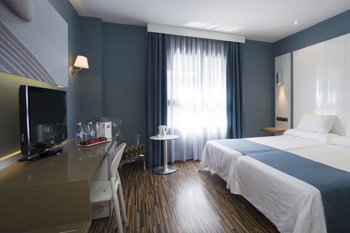 A hotel room with a bed, a TV, a desk, and a chair.