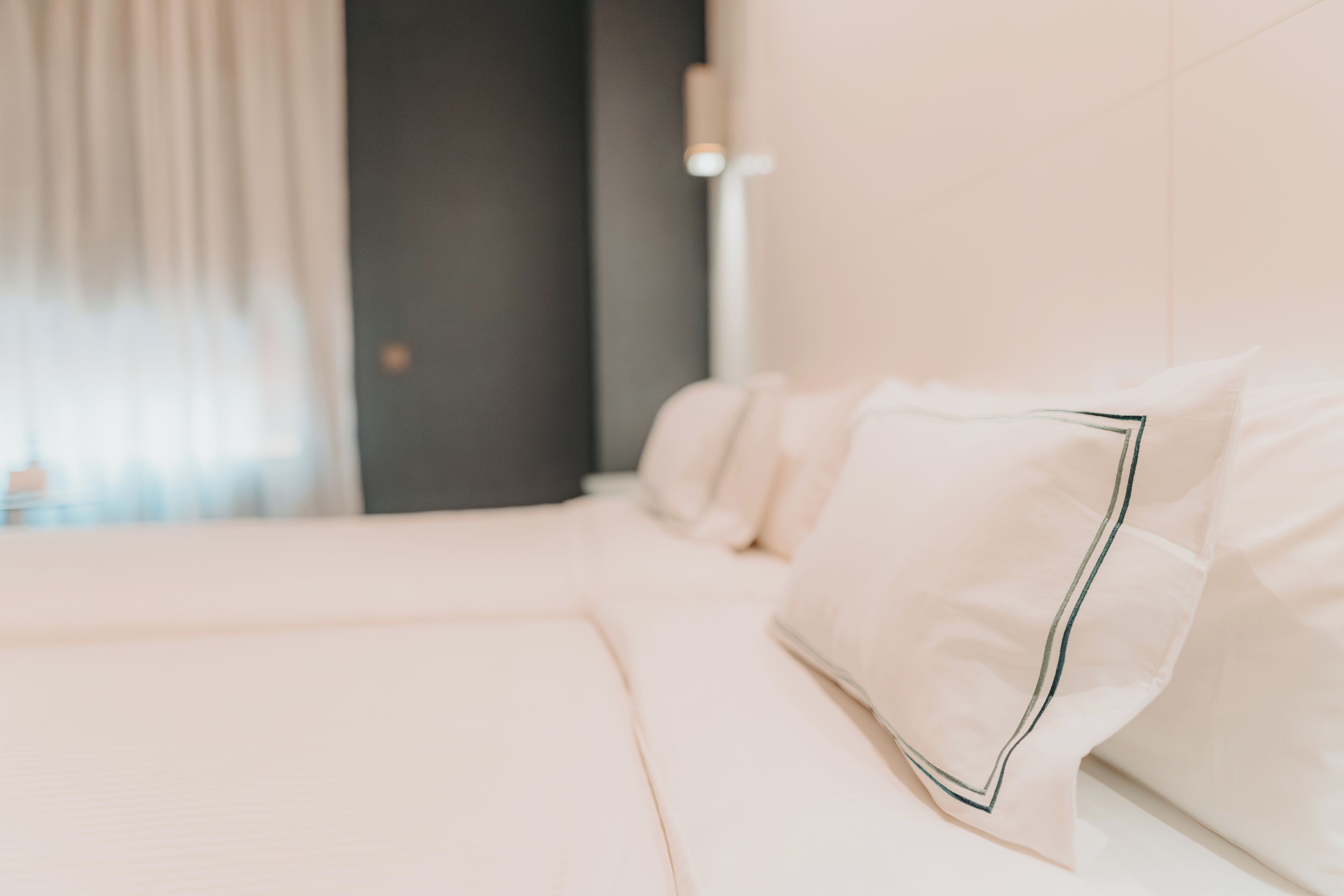A neatly made bed with white linens and a pillow with a dark trim.