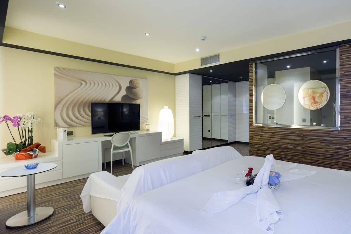 A modern hotel room with a large bed, a desk with a chair, a TV, and a mirror.