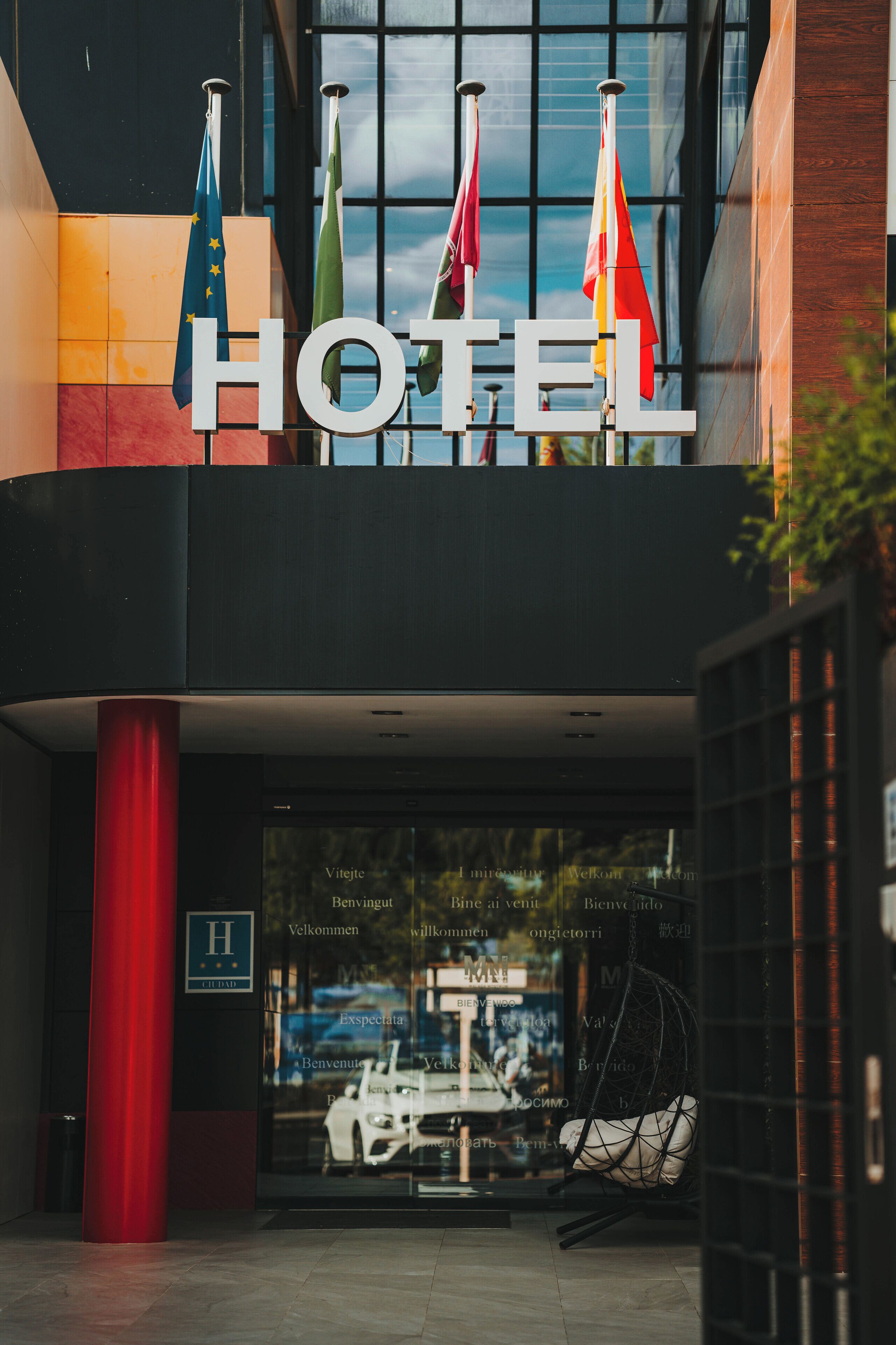Entrada de hotel con banderas, un letrero y una puerta de vidrio.