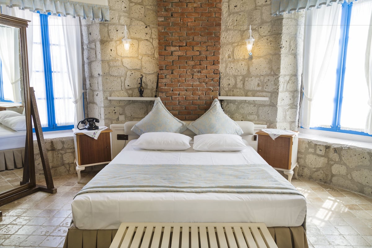 A bedroom with a large bed, a brick wall, stone walls, and a window with blue curtains.