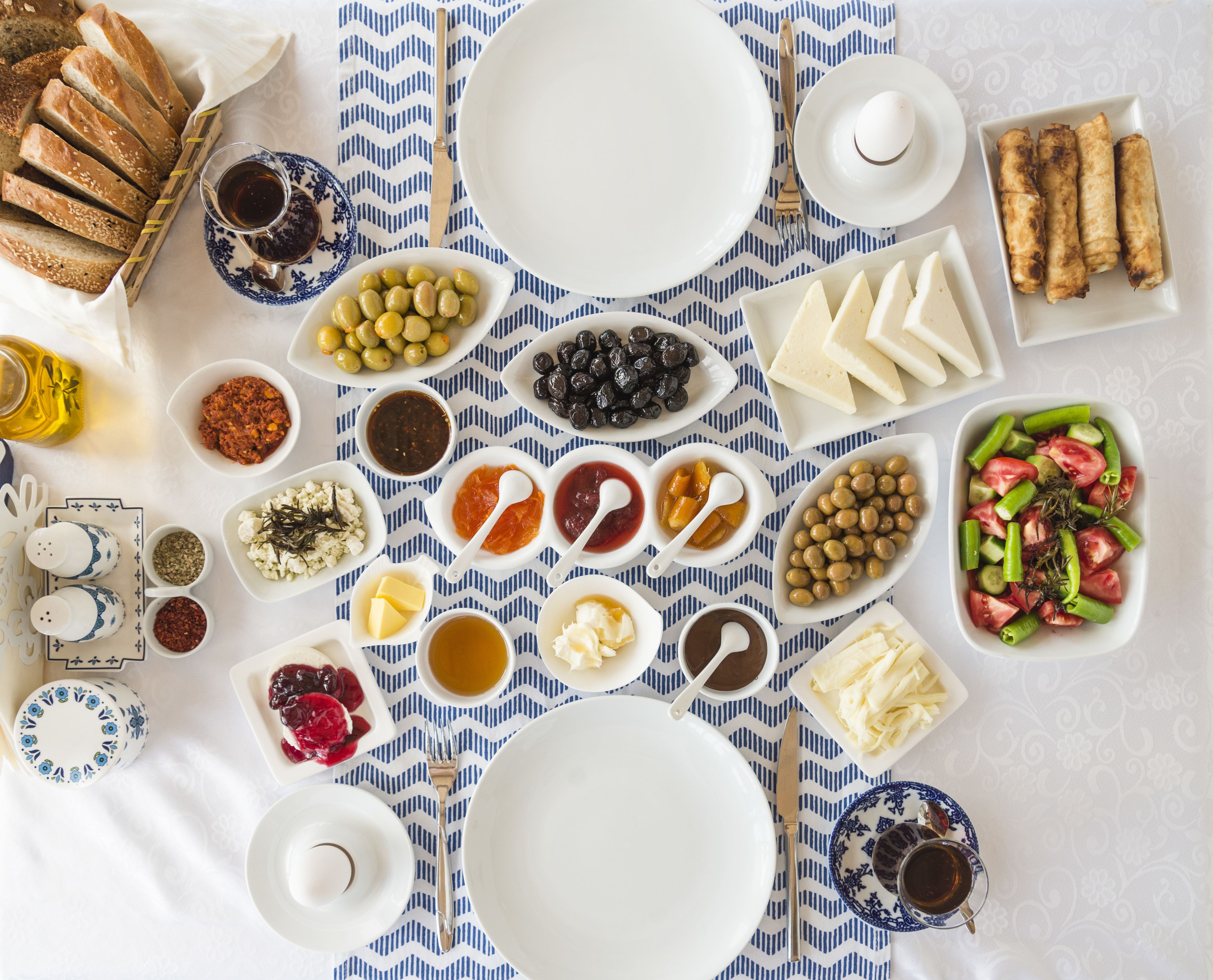 Une table dressée avec divers aliments et ustensiles, notamment du pain, des olives, du fromage et une salade.