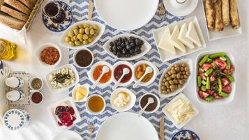 Une table dressée avec divers aliments et ustensiles, notamment du pain, des olives, du fromage et une salade.