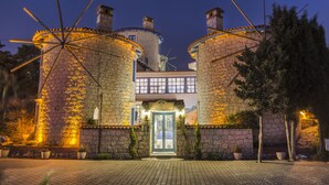 A stone building with a central entrance and two cylindrical towers, each with a windmill on top. - Alacati Degirmen Otel (Cesme)