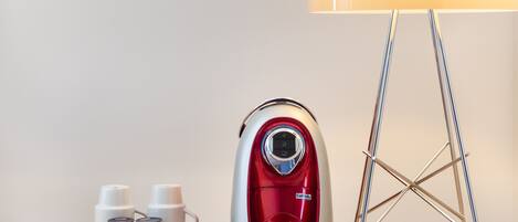 A red and silver electric kettle on a tray with two white cups and a small container, next to a lamp and a metal stand.