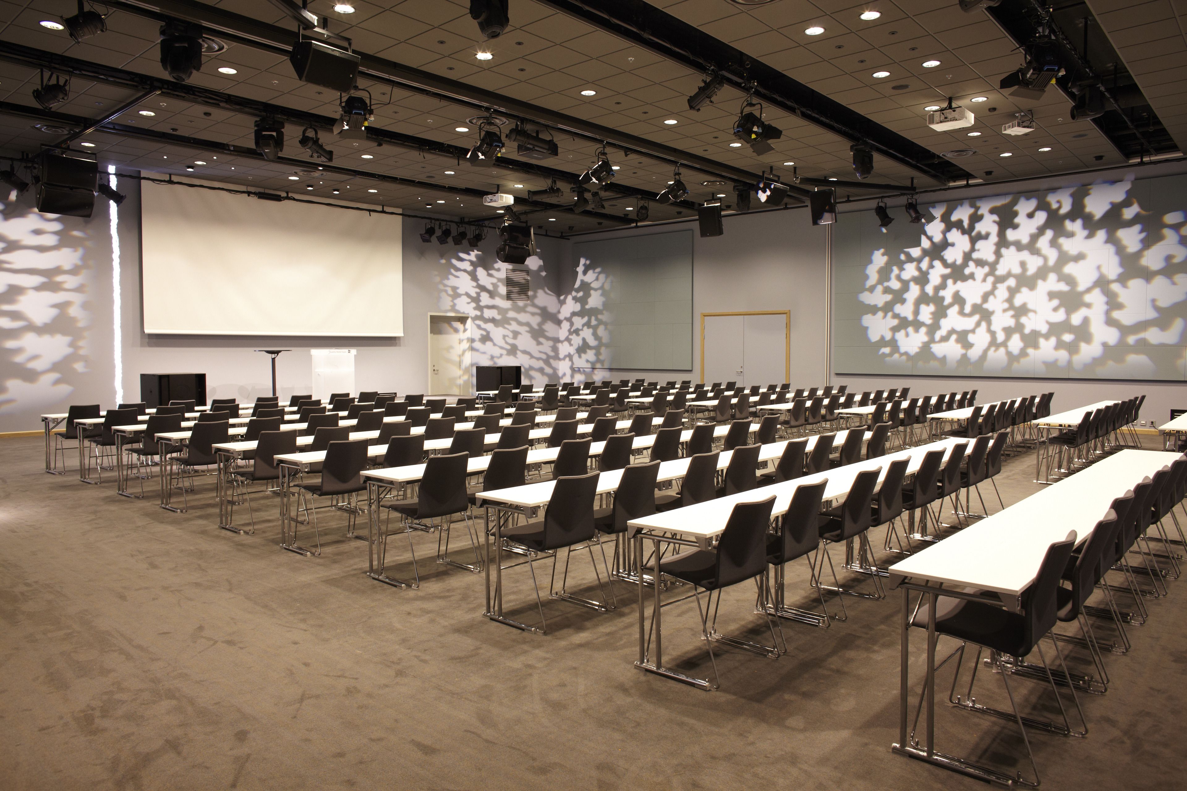 A conference room with rows of tables and chairs, a large screen, and a projector.