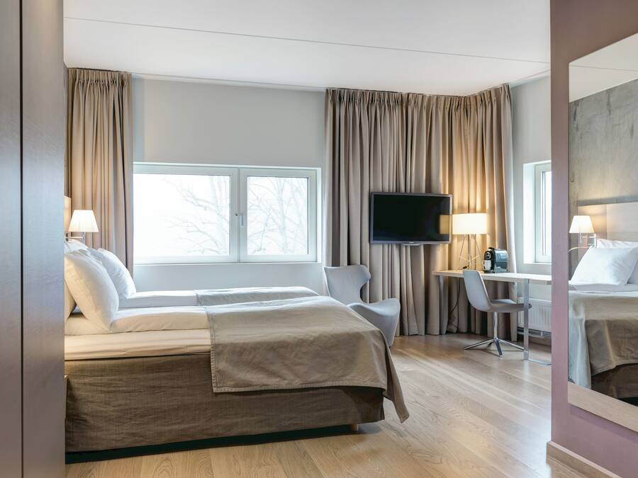 A hotel room with a large bed, a desk with a chair, a television, and a window with curtains.