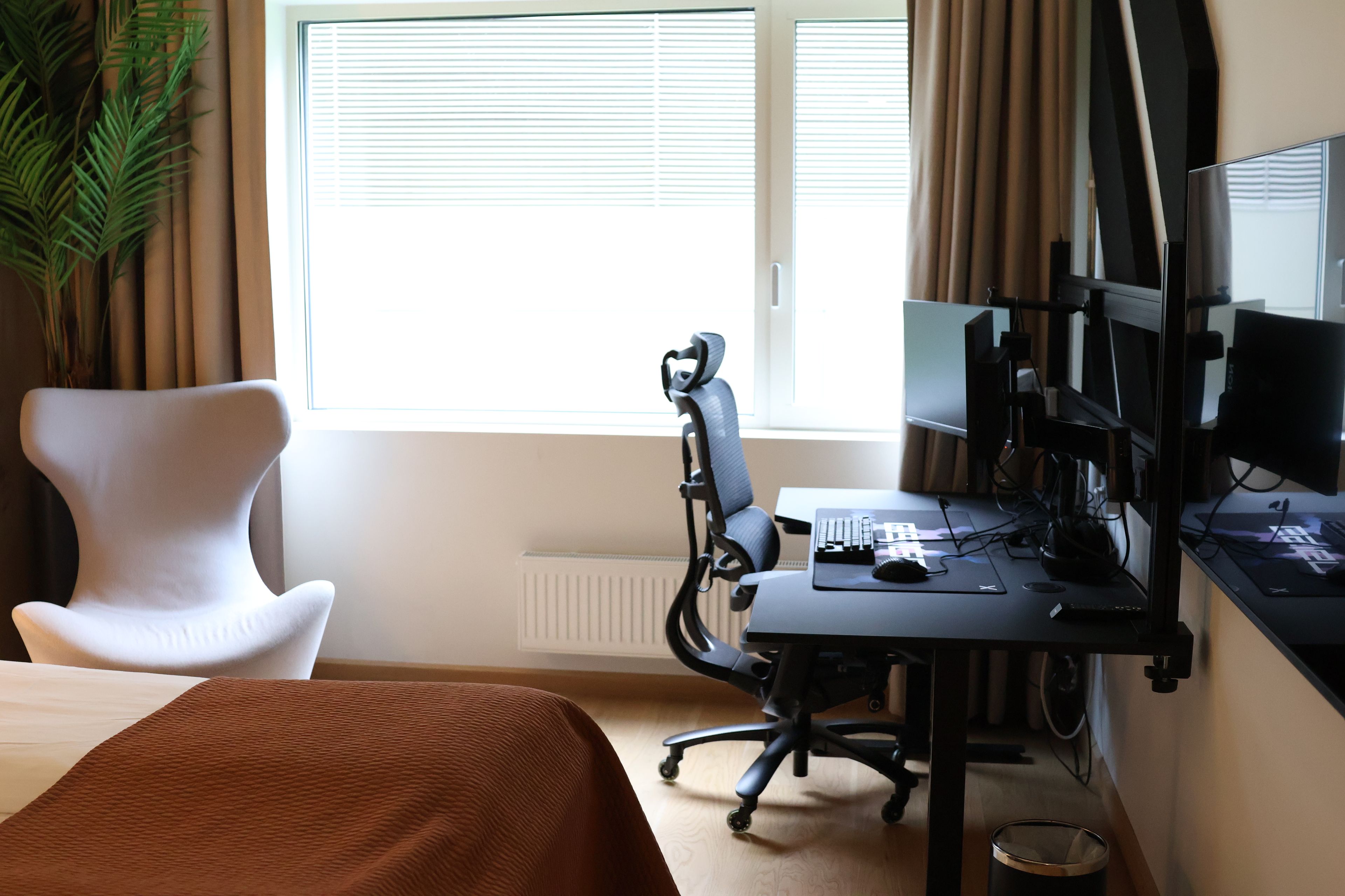 A hotel room with a bed, a desk with a computer, a chair, and a window with curtains.