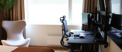 A hotel room with a bed, a desk with a computer, a chair, and a window with curtains.