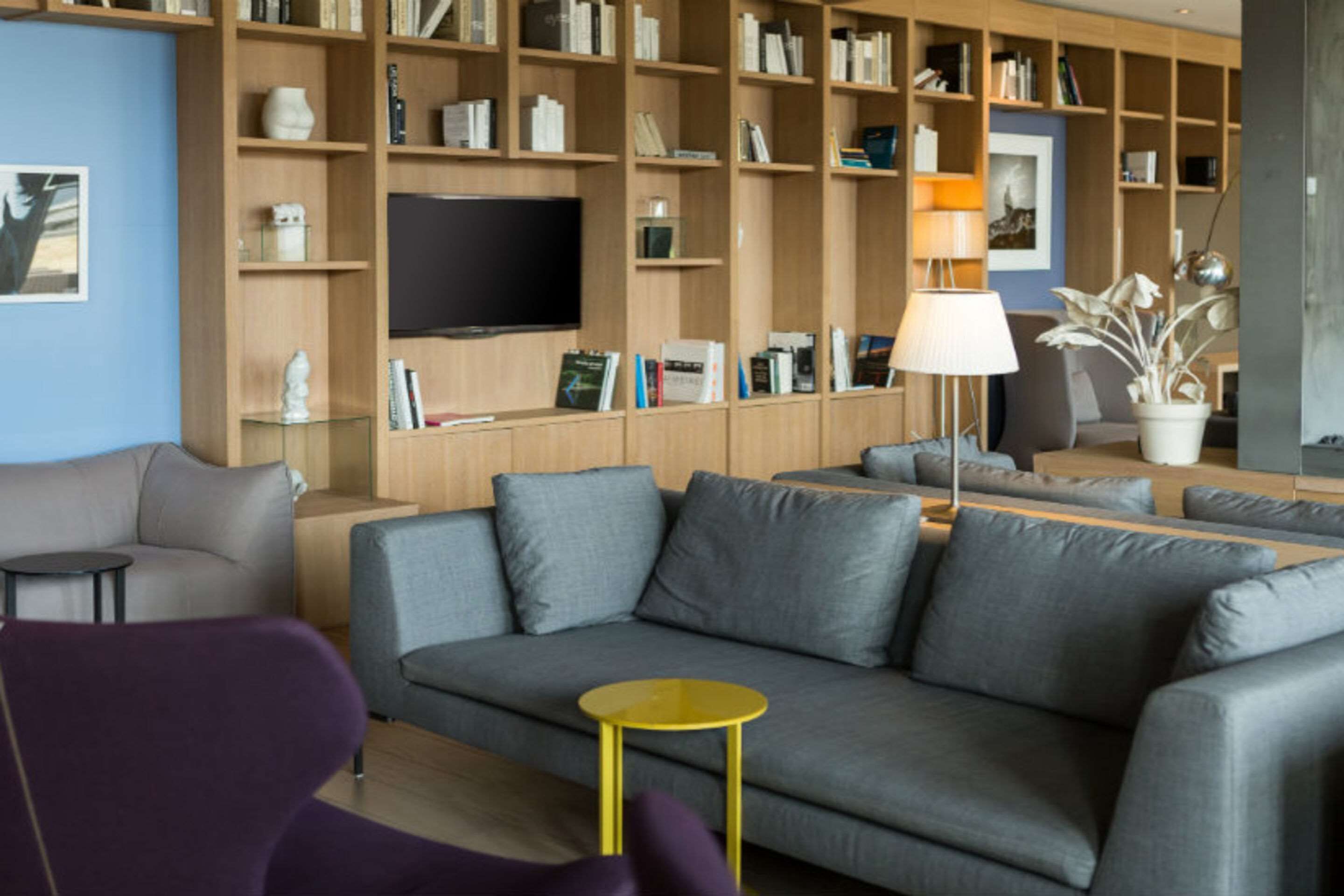 A modern living room with a grey sofa, a yellow side table, and a bookshelf filled with books and decorative items.