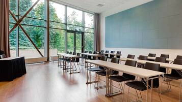 Un salón de conferencias con largas mesas y sillas, ventanas amplias y una pantalla para proyector.