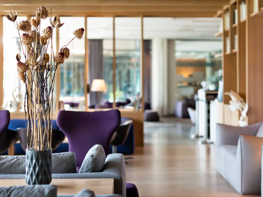 Un rebedor d'hotel modern amb un gran vas de flors seques, seients confortables i una vista de la ciutat a través de grans finestres.