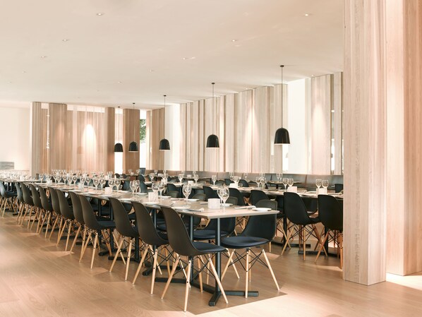 Un comedor moderno con mesas largas, sillas negras e iluminación colgante.