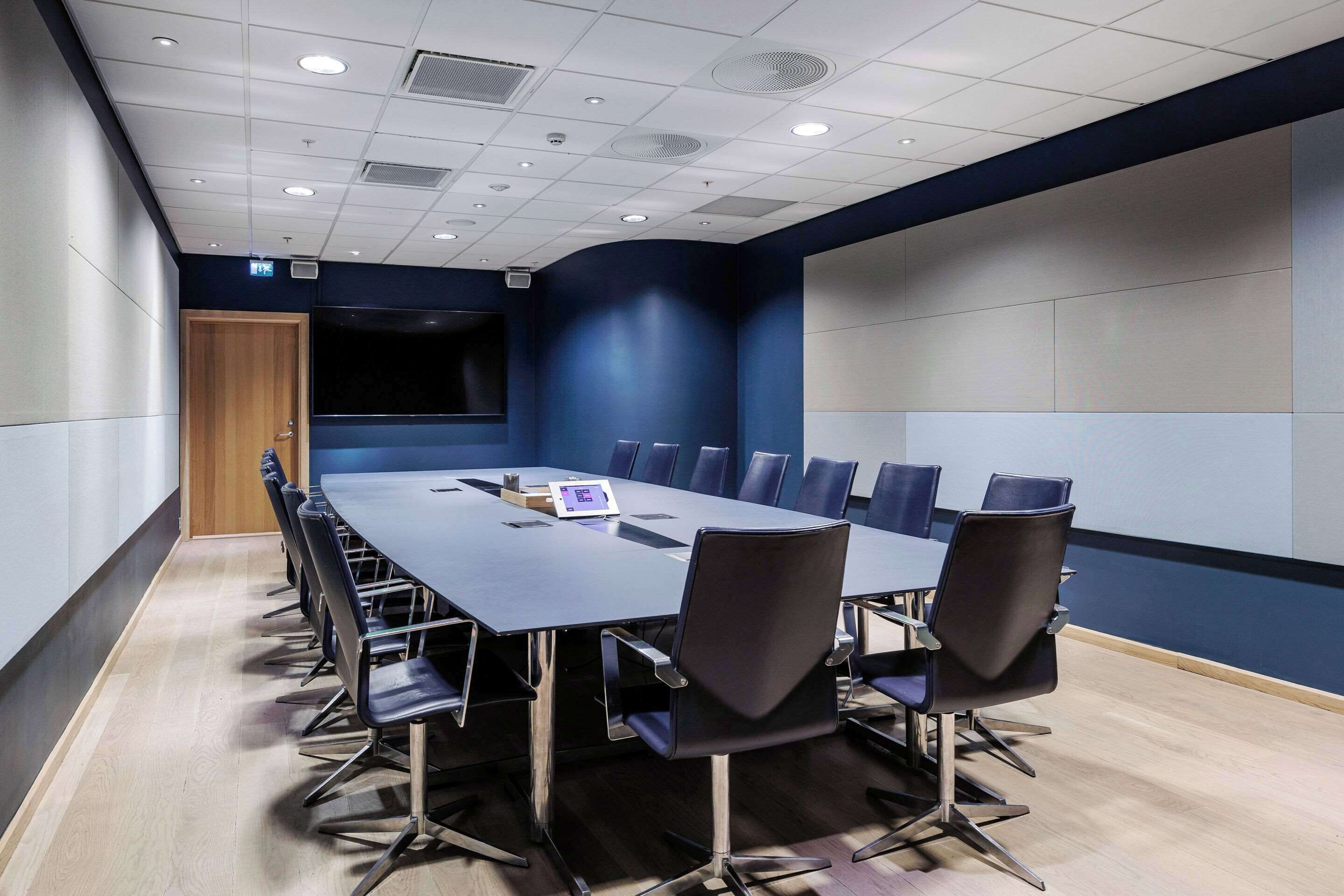 A conference room with a long table, chairs, and a projector screen.