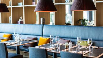 Een restaurant met houten planken, een blauwe met kussens bekleedde bank en tafels gedekt met wijnglazen en bestek.