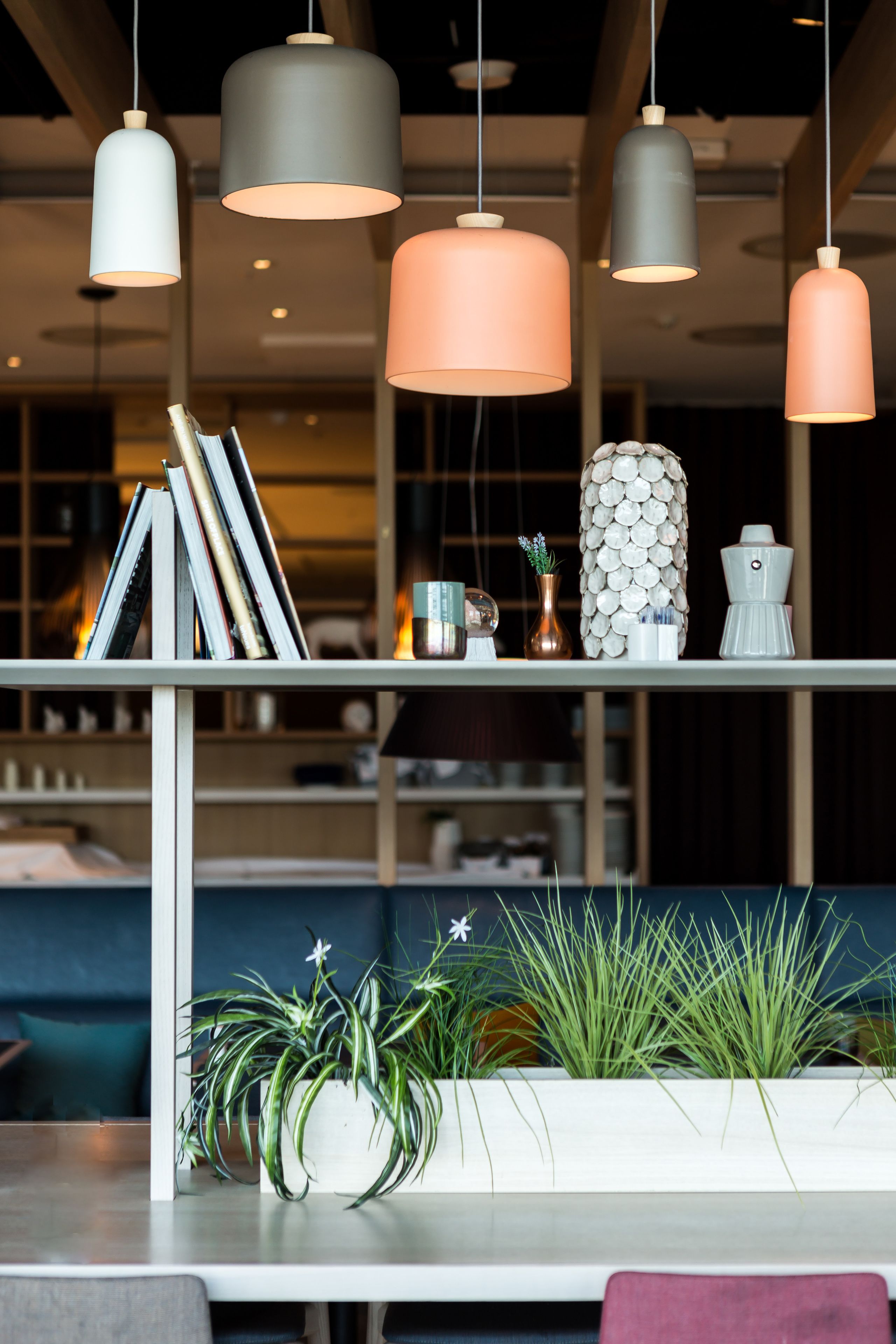Um interior moderno com iluminação pendente, estante de livros, vasos decorativos e plantas em vasos.