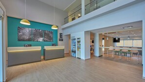 A modern reception area with a teal accent wall, two reception desks, a vending machine, and a seating area with tables and chairs. - City Express by Marriott Playa Del Carmen (Playa del Carmen)