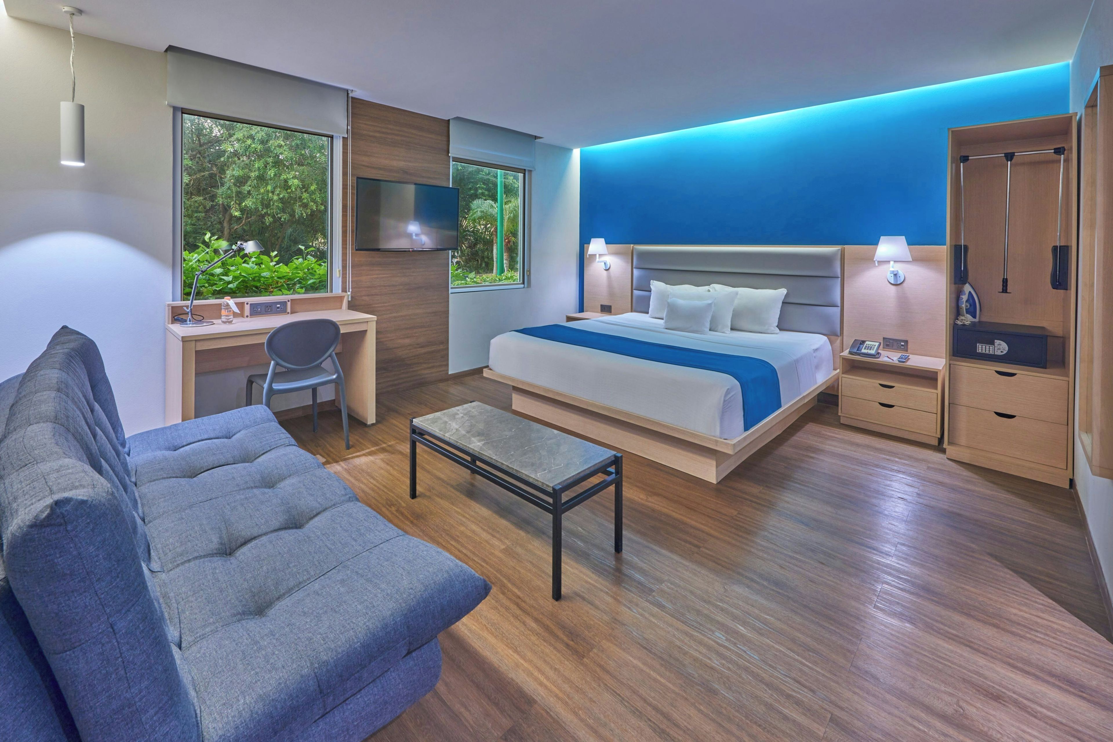 A modern hotel room with a bed, desk, chair, and a sofa.
