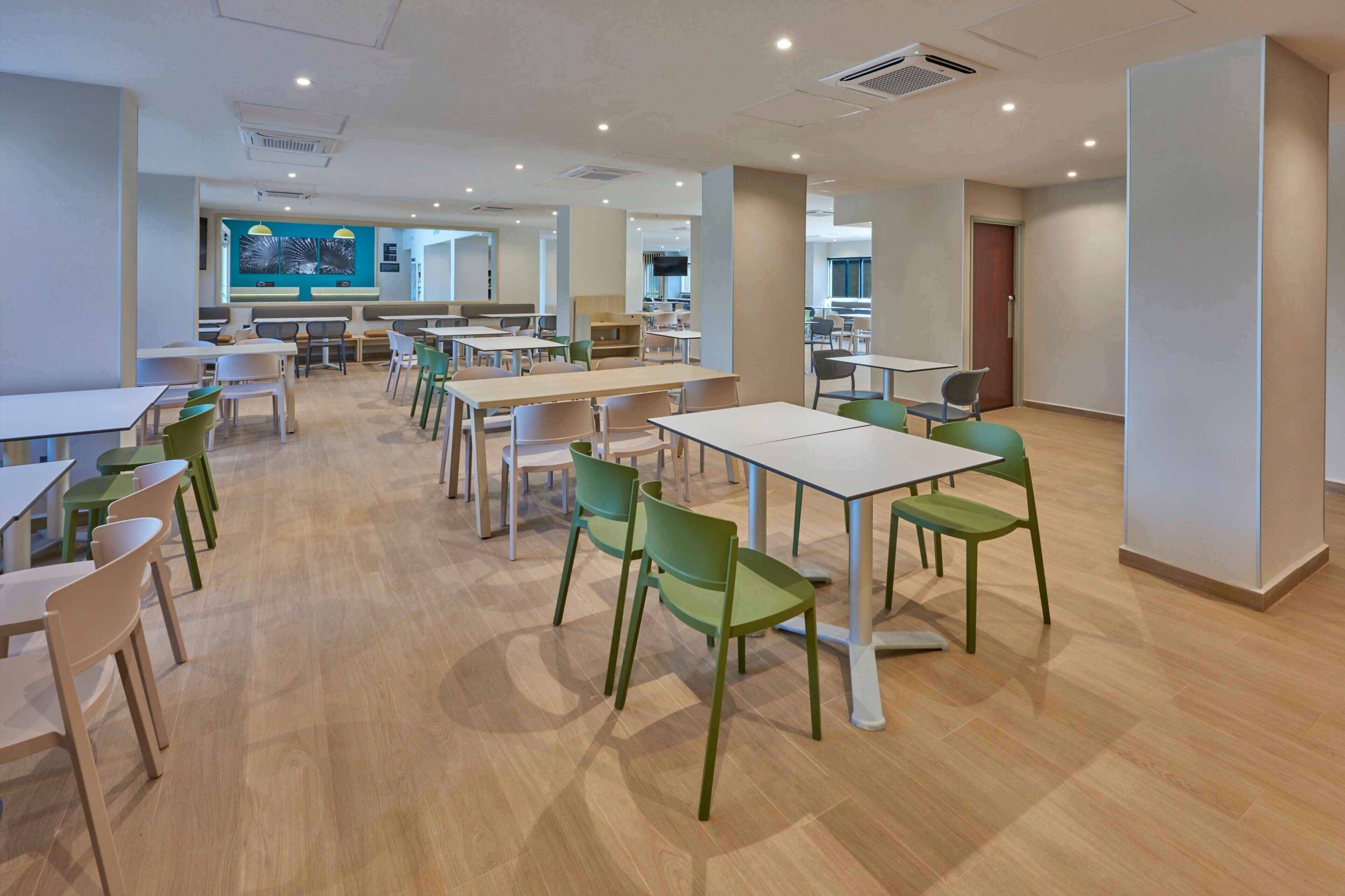 Un amplio comedor interior con múltiples mesas y sillas, una cocina al fondo y un diseño moderno.
