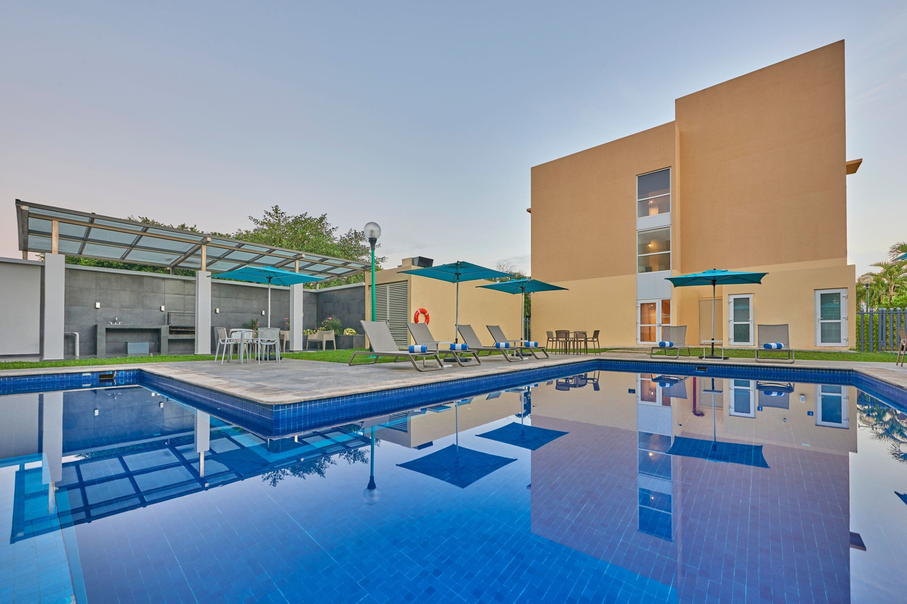 A swimming pool with lounge chairs and umbrellas, a covered patio area, and a building with a modern design.