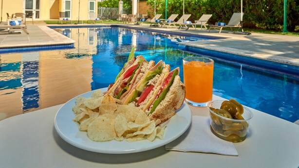 A poolside dining setup with a plate of chips, a sandwich, a drink, and a small bowl of olives. - City Express by Marriott Playa Del Carmen (Playa del Carmen)