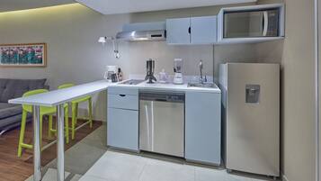 Cozinha compacta com máquina de lavar louça, micro-ondas e frigorífico. Inclui mesa de jantar com cadeiras, máquina de café e liquidificador.