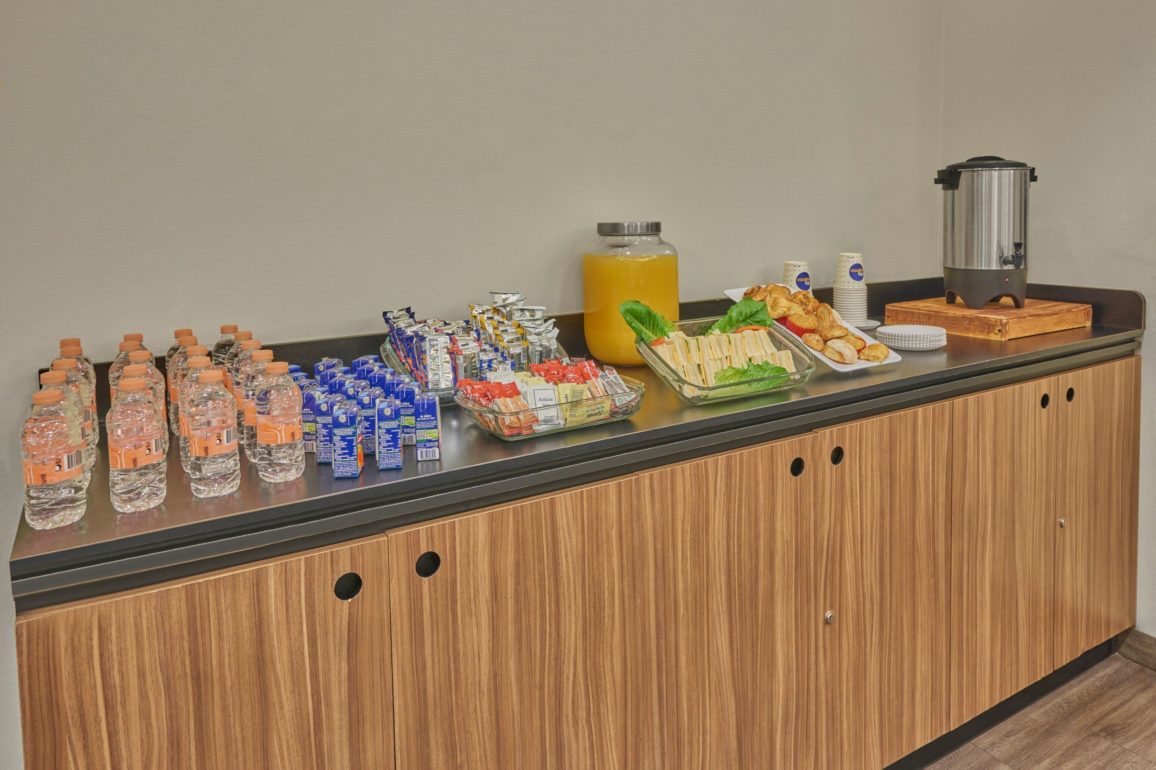 Un mostrador de buffet con diferentes alimentos, botellas de agua y una cafetera.