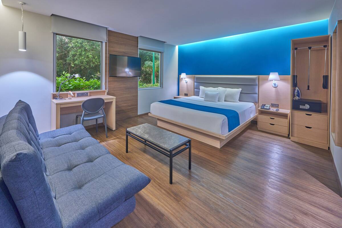 Habitación de hotel moderna con una cama grande, un escritorio, un sofá y vistas a zonas verdes.