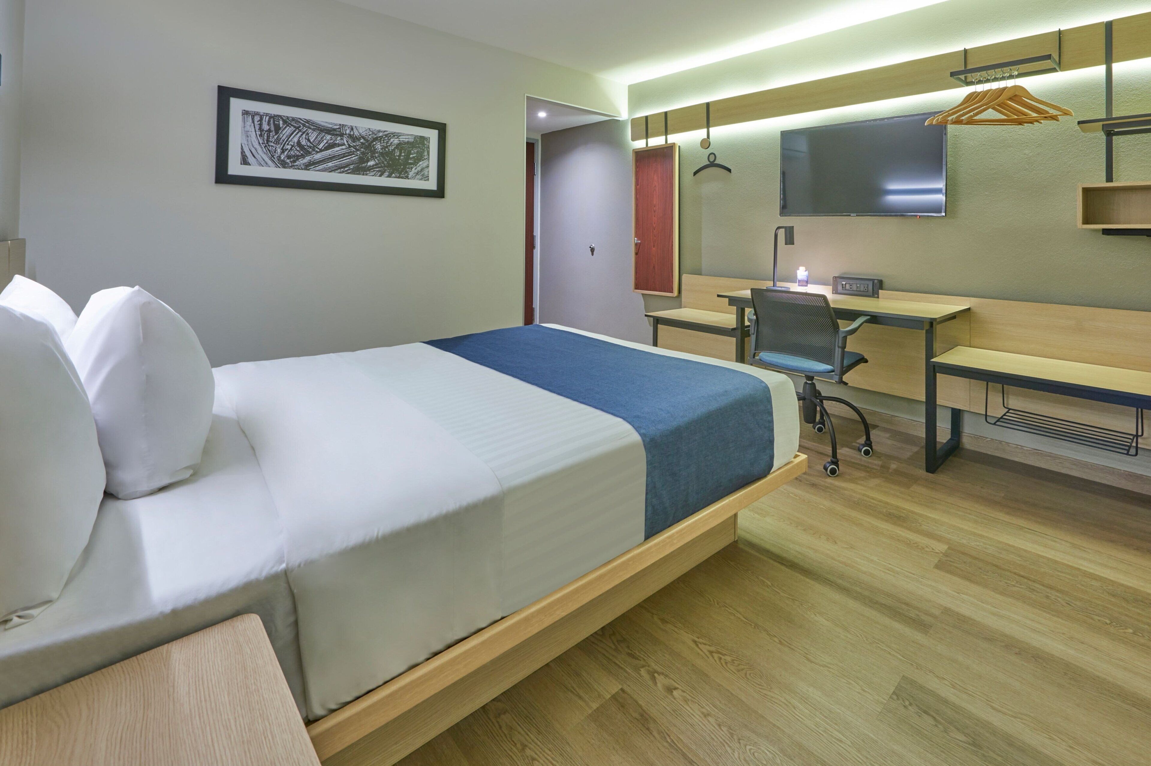 Een hotelkamer met een bed, bureau, stoel, televisie en een kledingkast.