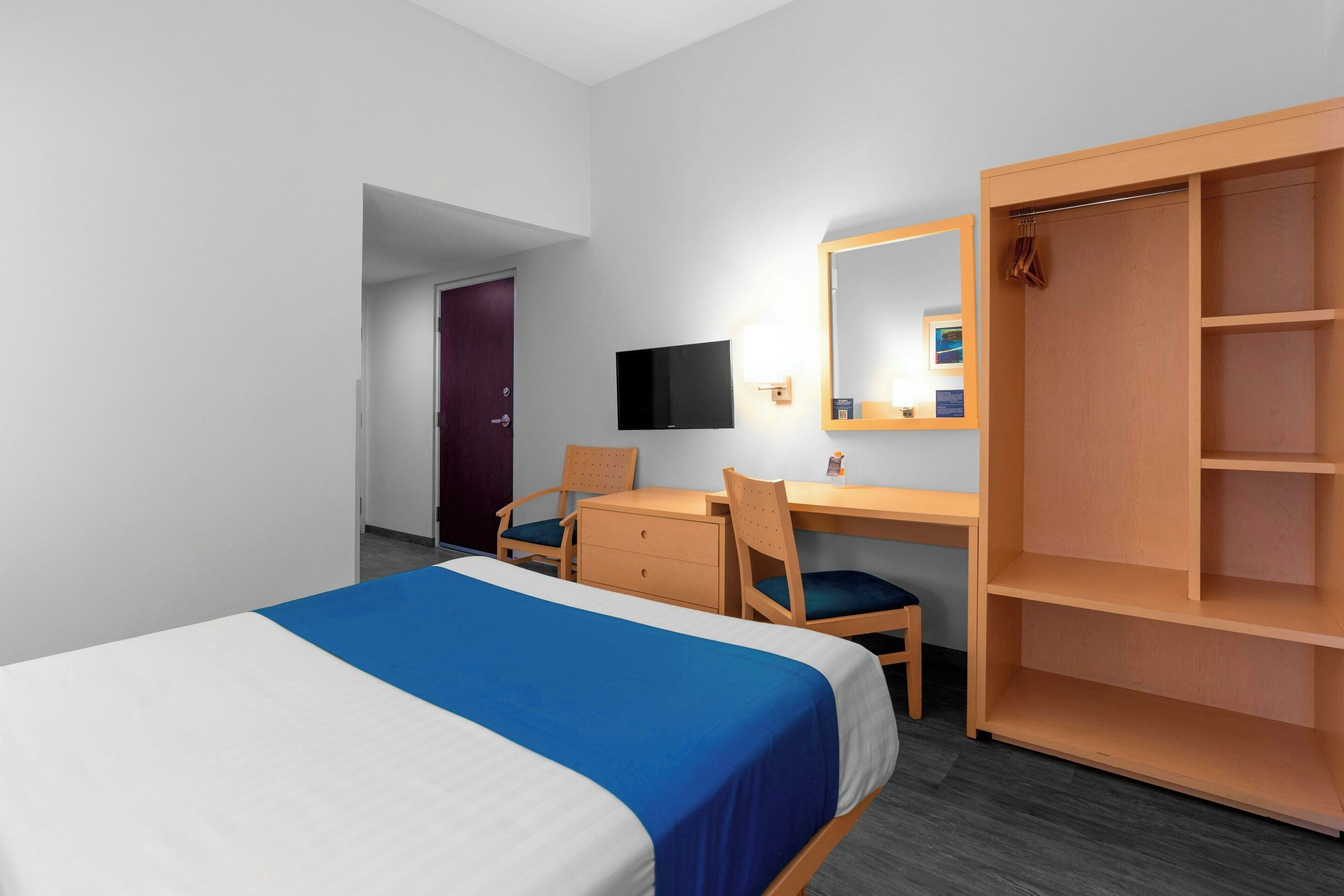 Een hotelkamer met een bed, een bureau, een stoel, een kledingkast, een televisie en een spiegel.