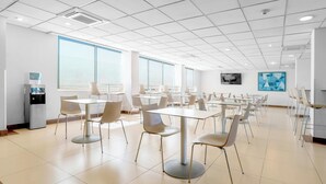Un grand espace dédié à la salle à manger, avec plusieurs tables et chaises, de grandes fenêtres et un réfrigérateur.