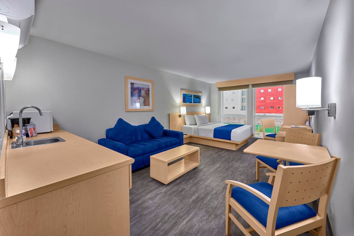 Una habitación de hotel moderna con kitchenette, un sofá azul, una cama y un comedor.