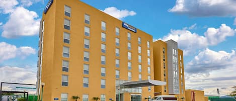 A CityExpress Hotel with a yellow facade, multiple floors, and a covered entrance.