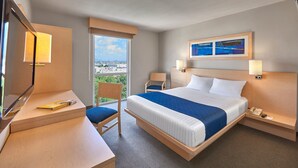 A hotel room with a bed, desk, chair, and a large window offering a city view. - City Express by Marriott Puebla Finsa (Cuautlancingo)