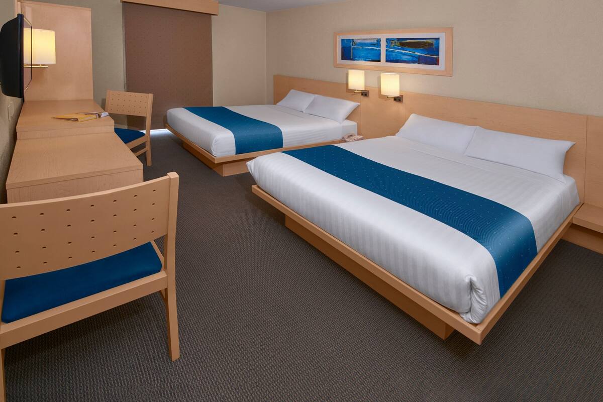 A hotel room with two beds, a desk, and a chair.