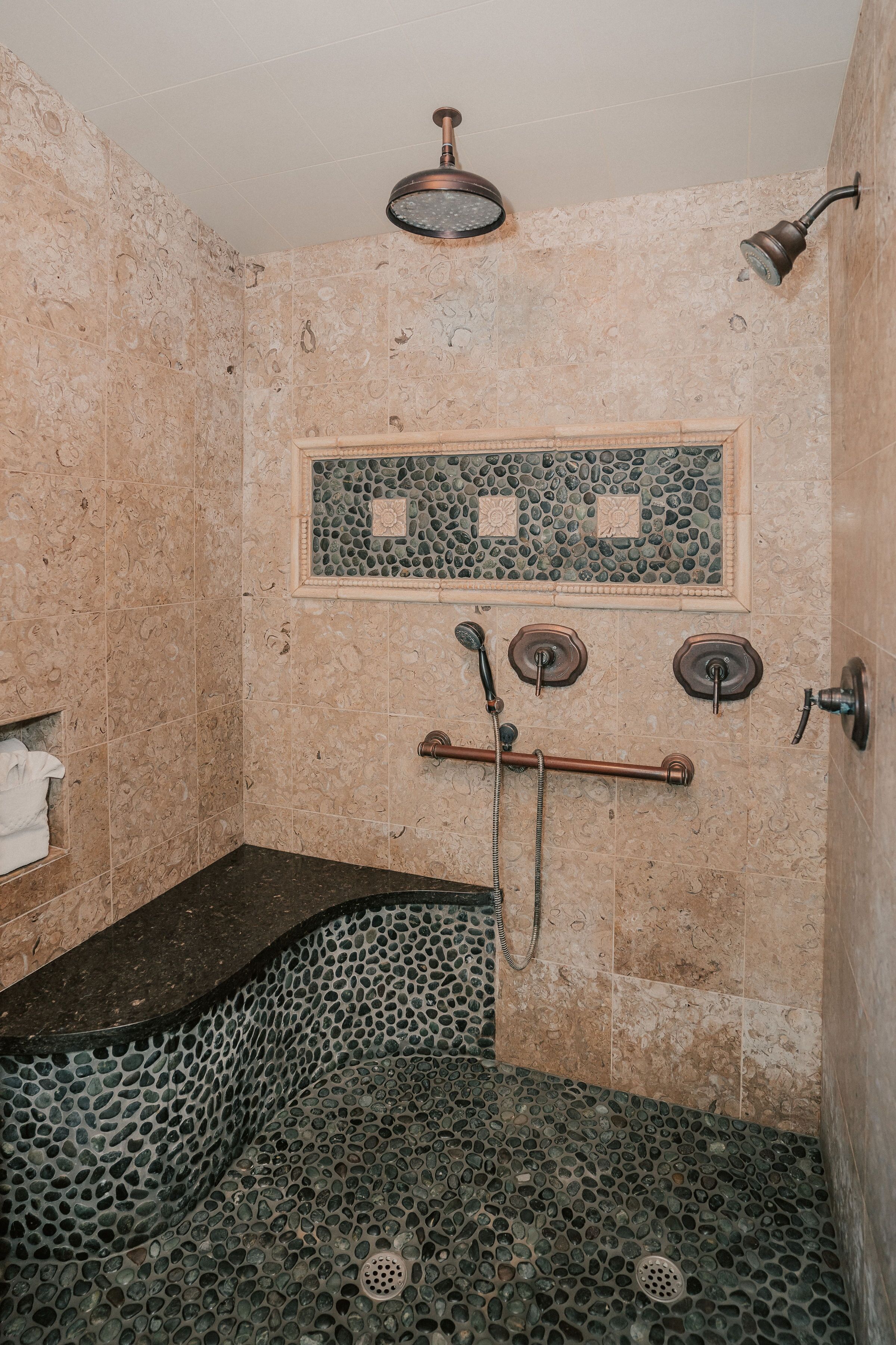 Un baño con piso de mosaico de piedra, ducha con cabezal de ducha manual y perchero.