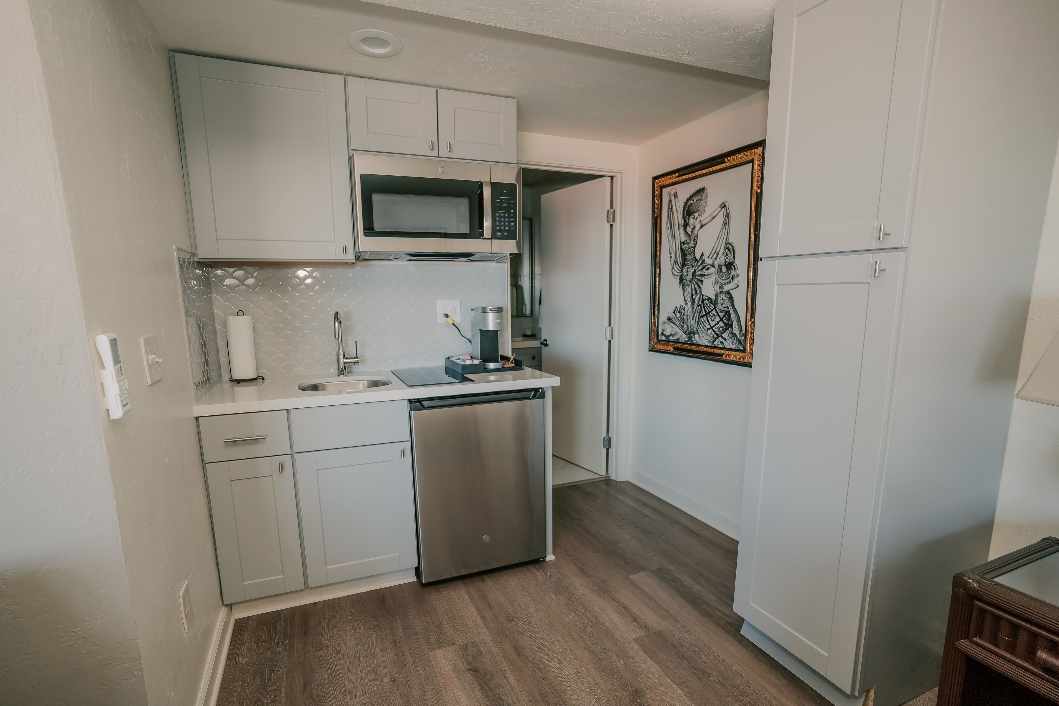 A compact kitchen with white cabinets, a stainless steel dishwasher, a microwave, and a coffee maker.