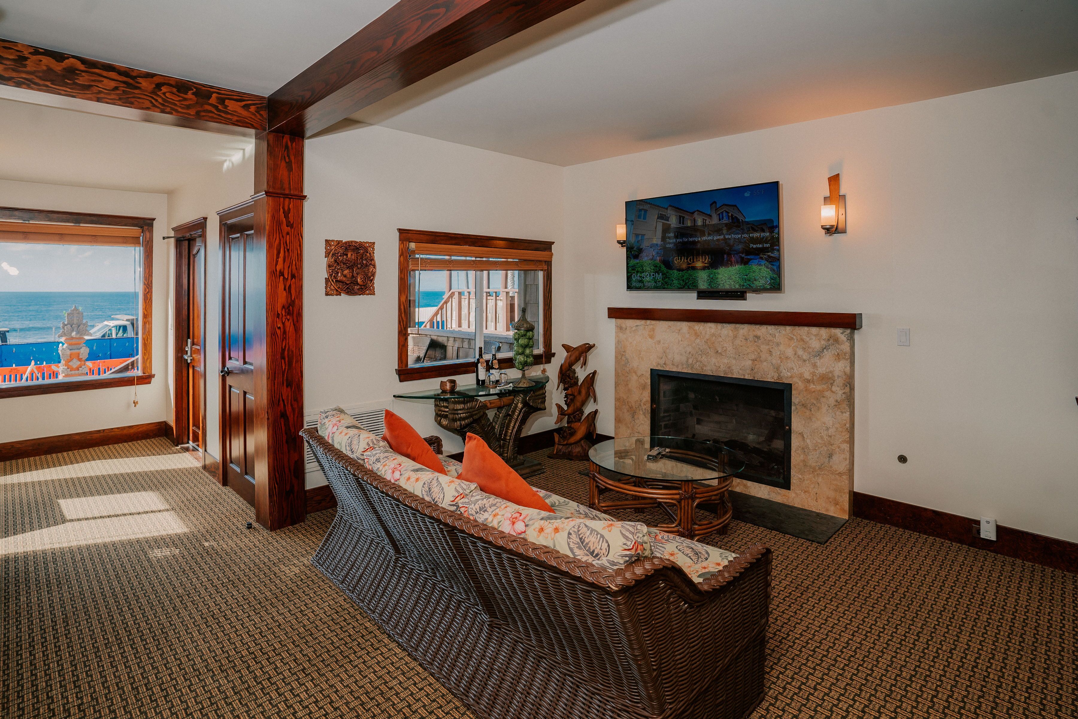 A living room with a wicker sofa, a fireplace, a television mounted on the wall, and a view of the ocean through a large window.