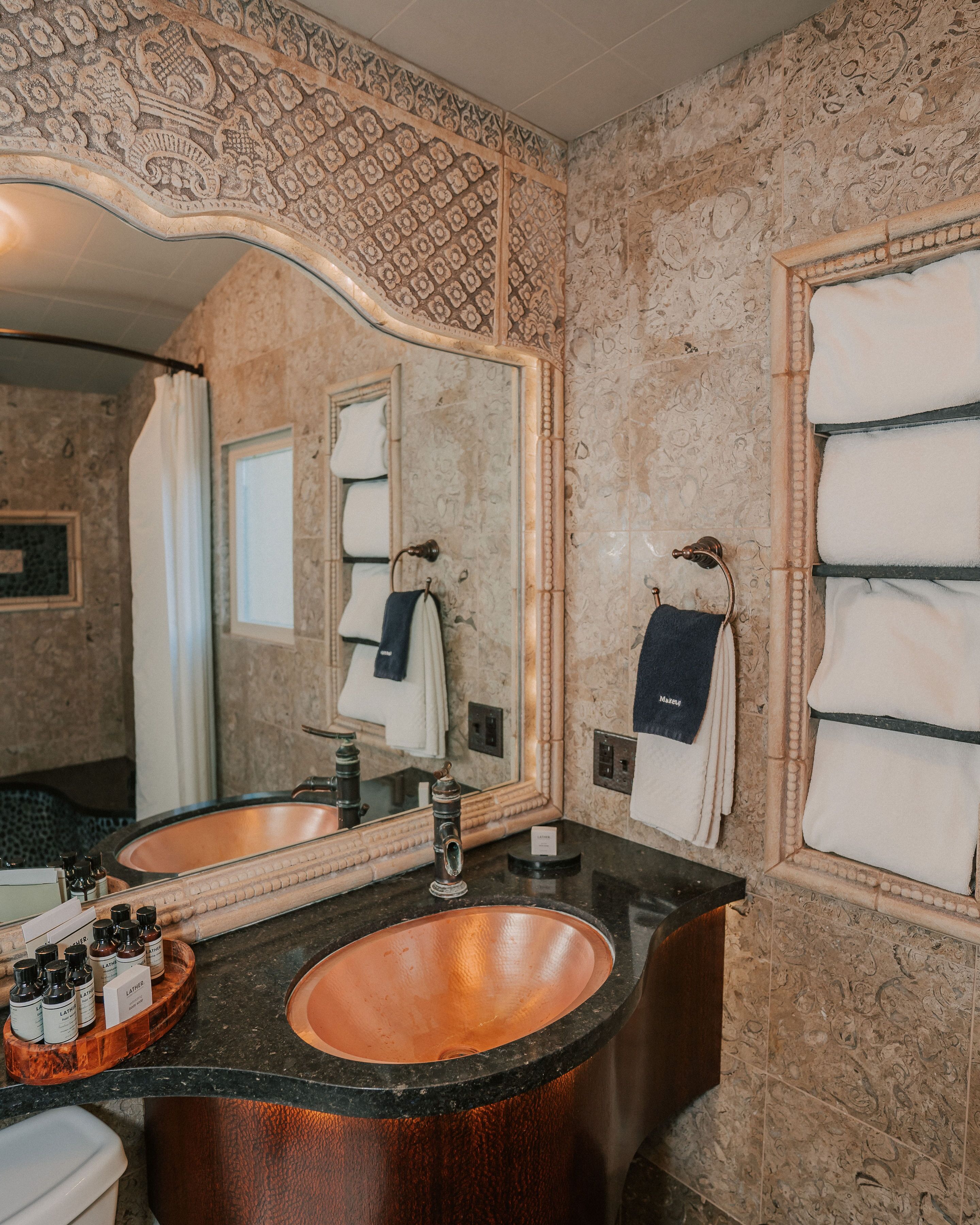 A bathroom with a large mirror, two sinks, and a vanity with a copper basin.