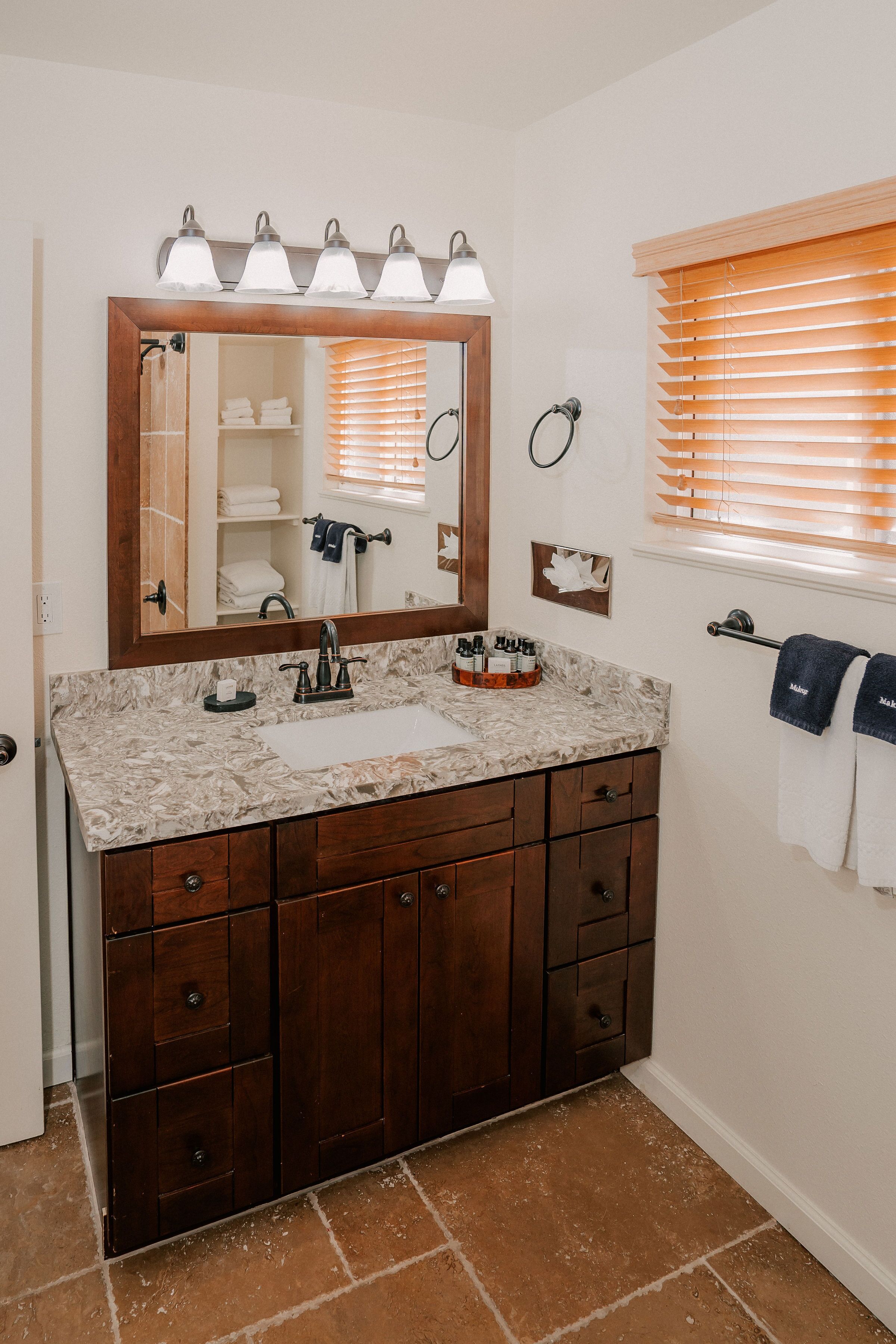 Un bagno con lavabo in marmo, mobile contenitore in legno e specchio con illuminazione.